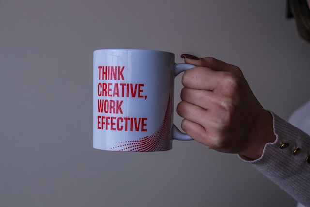 lady holding a white mug with the words think creative, work effective